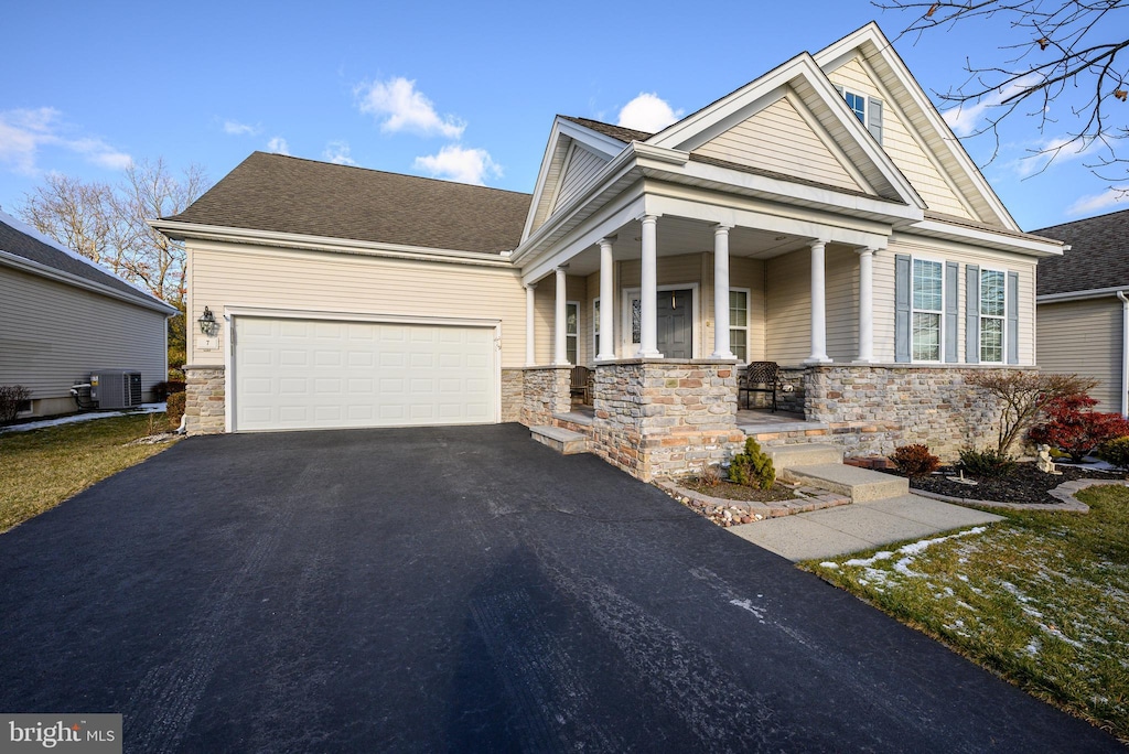 craftsman house with a porch, a garage, and central air condition unit