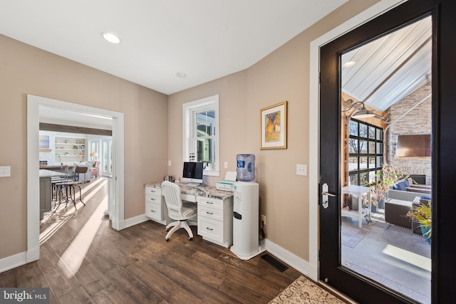 office featuring a stone fireplace, a healthy amount of sunlight, and dark hardwood / wood-style floors