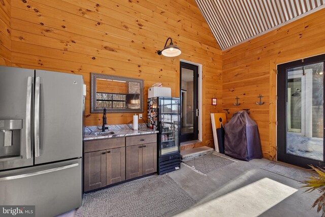 kitchen featuring wooden walls, concrete flooring, wine cooler, and stainless steel fridge