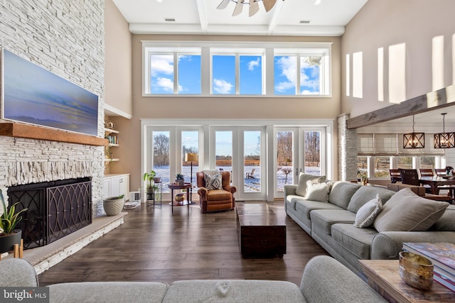 living room with a water view, beamed ceiling, dark hardwood / wood-style floors, a fireplace, and ceiling fan with notable chandelier