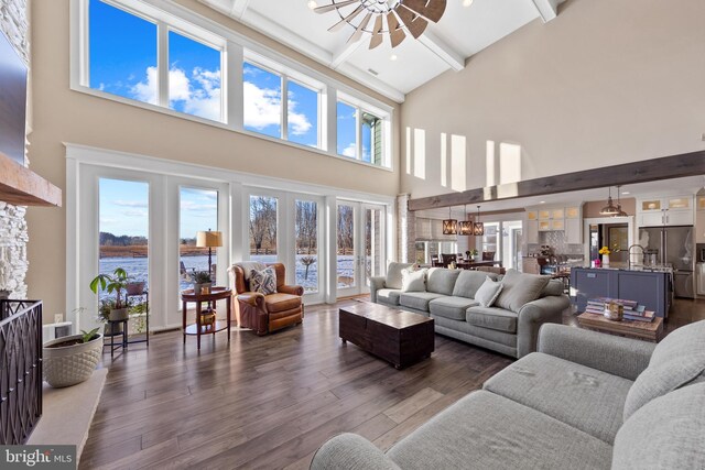 living room featuring a towering ceiling, dark wood-type flooring, a notable chandelier, and beam ceiling