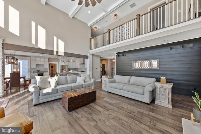 living room with a high ceiling, ceiling fan, beamed ceiling, and hardwood / wood-style floors