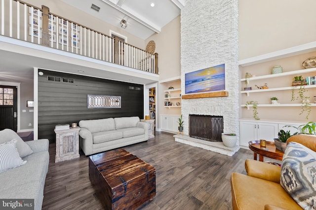 living room with beamed ceiling, dark wood-type flooring, a fireplace, a high ceiling, and built in features