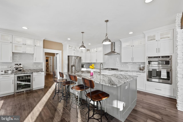 kitchen with a center island with sink, white cabinets, beverage cooler, and wall chimney exhaust hood