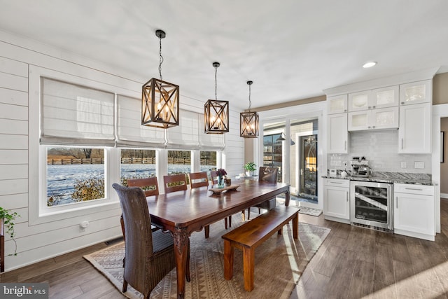 dining area featuring a healthy amount of sunlight, dark hardwood / wood-style flooring, wood walls, and wine cooler