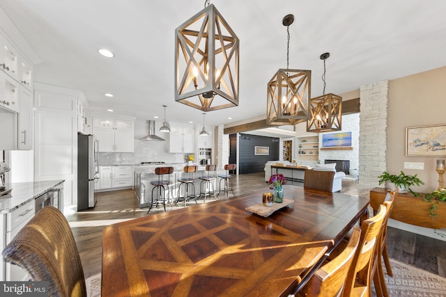 dining room with dark hardwood / wood-style floors, a notable chandelier, and a stone fireplace