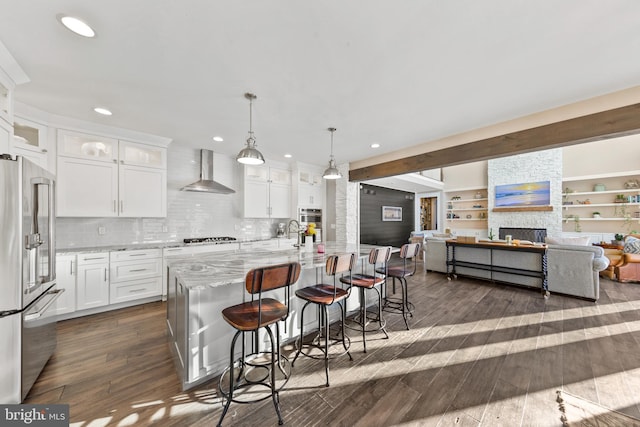 kitchen with white cabinetry, wall chimney exhaust hood, hanging light fixtures, high end refrigerator, and a stone fireplace