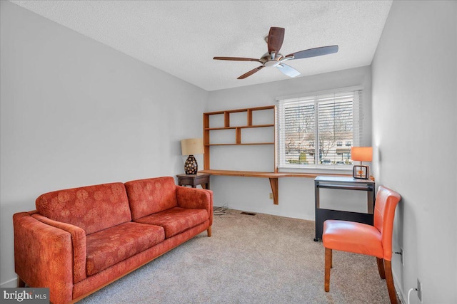 living area with a textured ceiling, light colored carpet, and ceiling fan