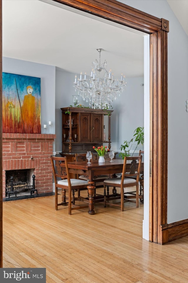 dining room with an inviting chandelier, light wood-type flooring, lofted ceiling, and a brick fireplace