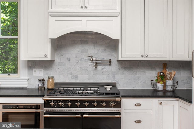 kitchen with tasteful backsplash, plenty of natural light, white cabinets, custom range hood, and appliances with stainless steel finishes