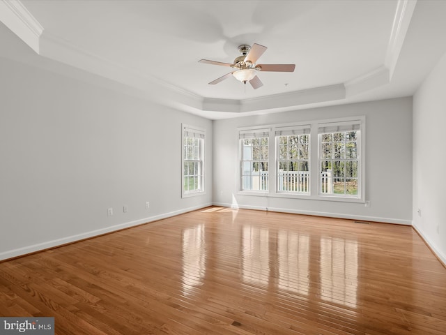spare room featuring a tray ceiling, wood finished floors, a ceiling fan, crown molding, and baseboards