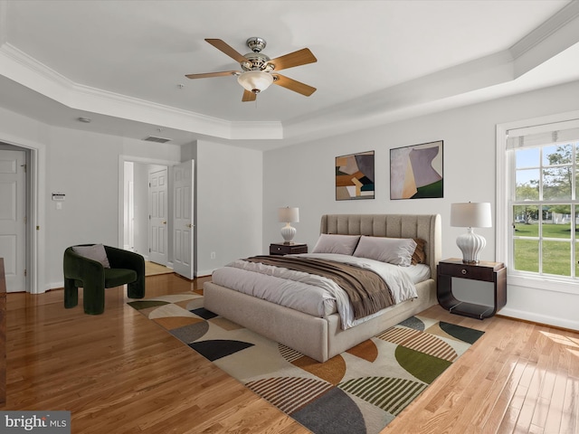 bedroom with visible vents, wood finished floors, a tray ceiling, and ornamental molding