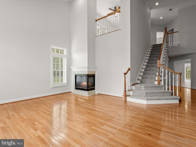 unfurnished living room featuring hardwood / wood-style flooring, baseboards, a high ceiling, and stairway