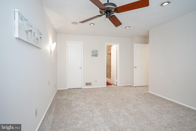 unfurnished bedroom featuring ensuite bathroom, a textured ceiling, ceiling fan, and light carpet