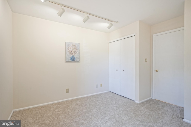 unfurnished bedroom featuring rail lighting, a closet, and light carpet