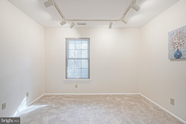 spare room with rail lighting and light colored carpet