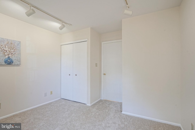 unfurnished bedroom with track lighting, light colored carpet, and a closet