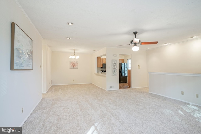 unfurnished living room with ceiling fan with notable chandelier, light carpet, and crown molding