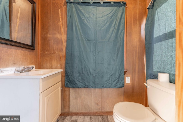 bathroom with toilet, wood walls, wood-type flooring, and vanity