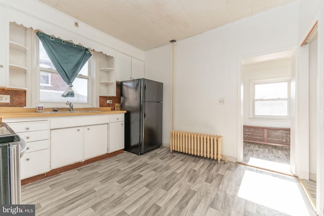 kitchen with sink, black fridge, white cabinetry, and radiator heating unit