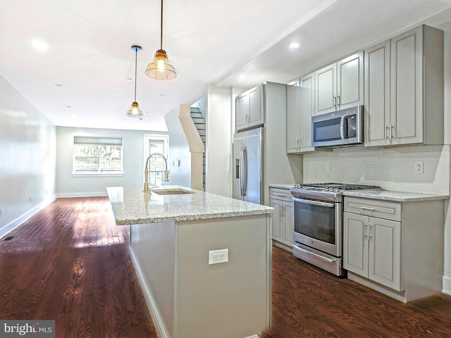 kitchen with stainless steel appliances, light stone countertops, an island with sink, and backsplash