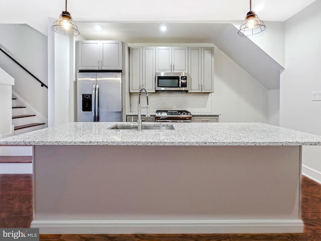 kitchen featuring sink, hanging light fixtures, light stone counters, stainless steel appliances, and a center island with sink