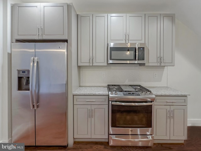 kitchen with tasteful backsplash, light stone counters, stainless steel appliances, and dark hardwood / wood-style floors