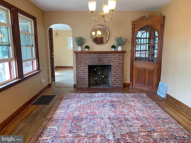 unfurnished living room featuring arched walkways, visible vents, an inviting chandelier, and wood finished floors