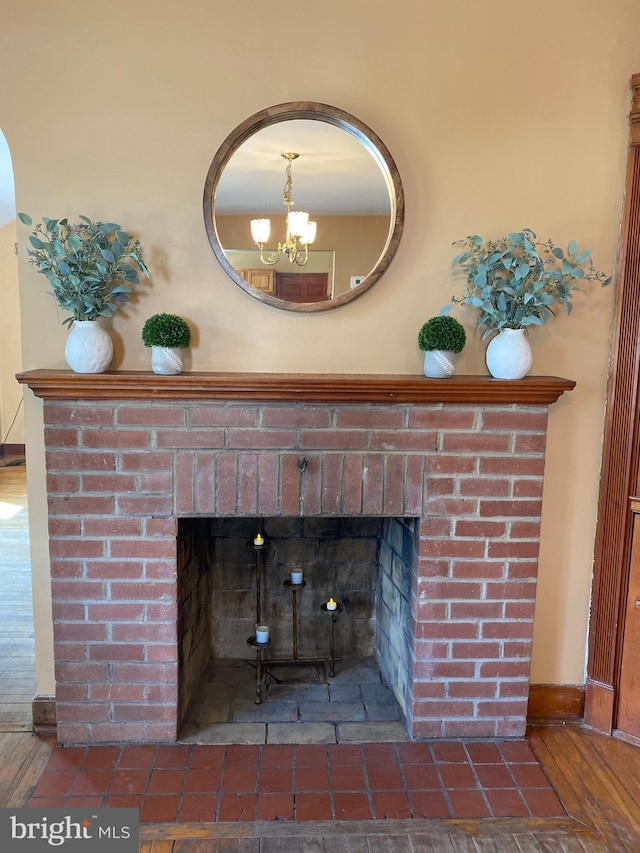 details featuring a chandelier, a brick fireplace, baseboards, and wood finished floors