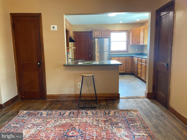 kitchen featuring baseboards, a peninsula, hardwood / wood-style floors, and freestanding refrigerator