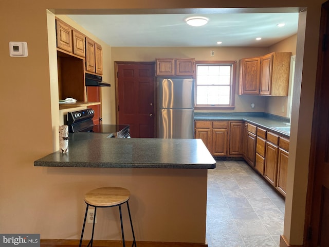 kitchen featuring a peninsula, freestanding refrigerator, electric range oven, under cabinet range hood, and dark countertops