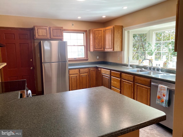 kitchen with a sink, dark countertops, recessed lighting, appliances with stainless steel finishes, and brown cabinetry