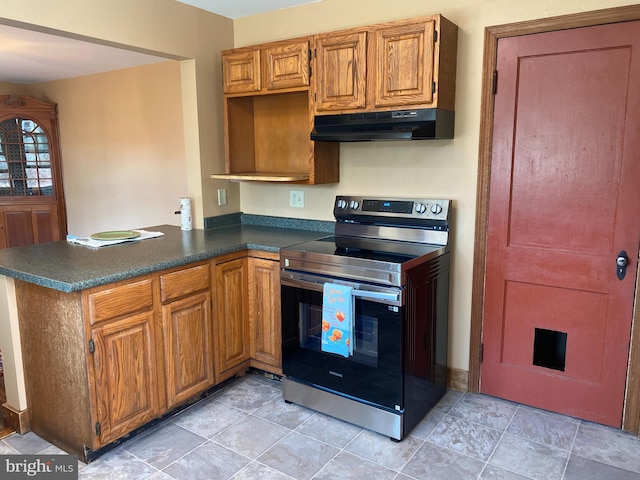 kitchen with dark countertops, under cabinet range hood, stainless steel electric range oven, brown cabinets, and a peninsula