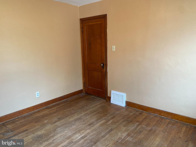 empty room featuring dark wood-style floors, visible vents, and baseboards