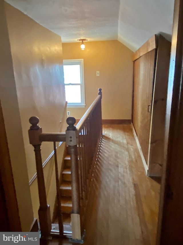 hall featuring lofted ceiling, wood finished floors, an upstairs landing, and baseboards