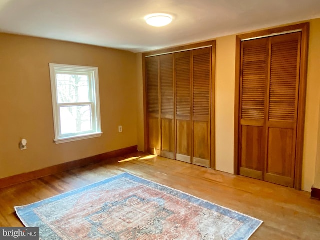 unfurnished bedroom featuring baseboards, two closets, and light wood finished floors