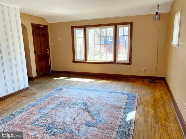 spare room featuring arched walkways, vaulted ceiling, baseboards, and hardwood / wood-style flooring