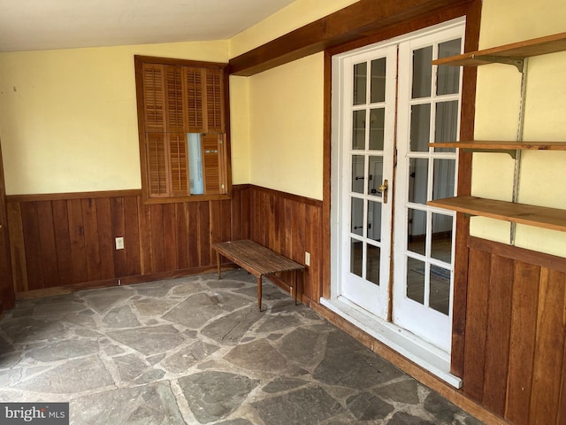 interior space with a wainscoted wall, lofted ceiling, stone floors, and wood walls