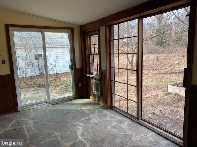 entryway with a wainscoted wall, heating unit, stone floors, and vaulted ceiling