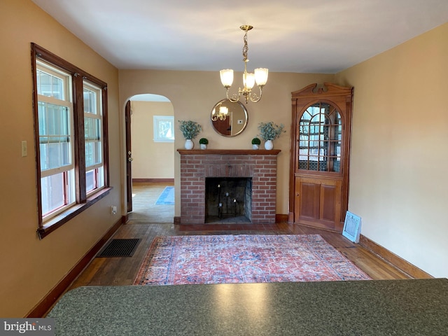 unfurnished living room with arched walkways, visible vents, an inviting chandelier, and wood finished floors