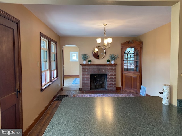 unfurnished living room with visible vents, a chandelier, a fireplace, arched walkways, and dark wood-style flooring