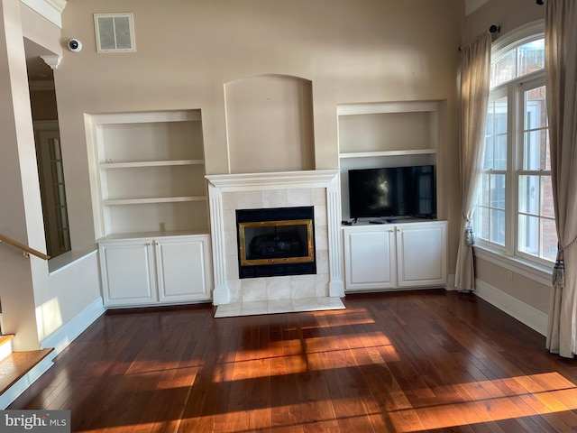 unfurnished living room with a tile fireplace, built in shelves, dark wood-type flooring, and a healthy amount of sunlight