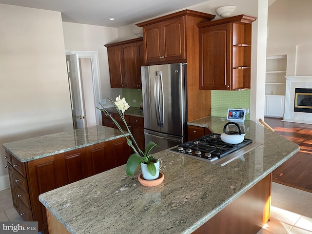 kitchen with light stone countertops, stainless steel appliances, a tile fireplace, and tasteful backsplash