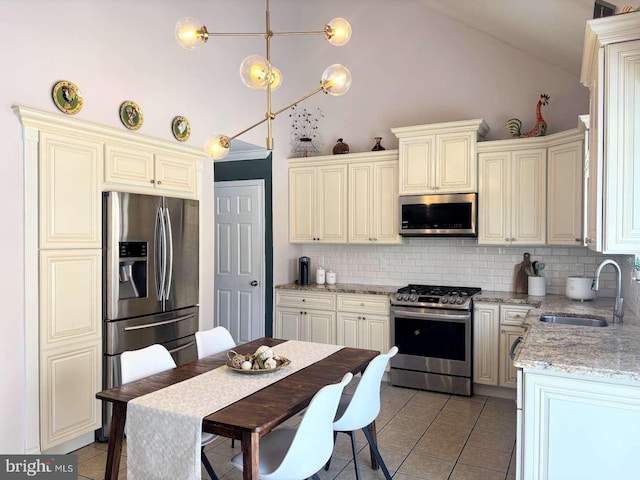 kitchen with sink, stainless steel appliances, cream cabinets, decorative light fixtures, and decorative backsplash