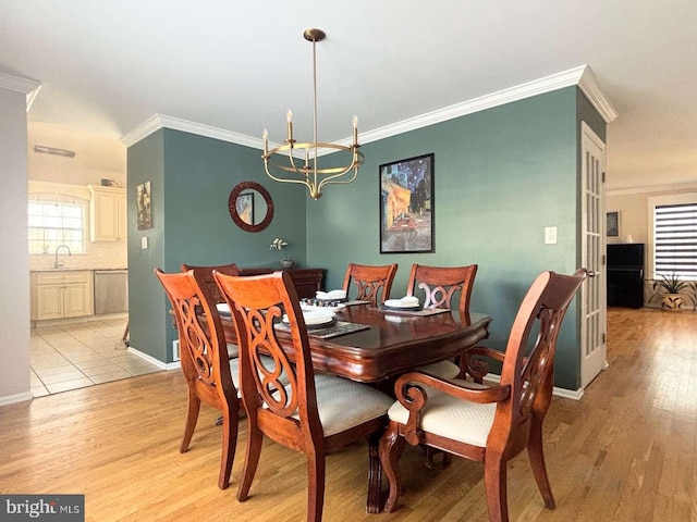 dining space featuring sink, ornamental molding, a notable chandelier, and light hardwood / wood-style flooring