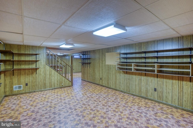 basement featuring wooden walls and a drop ceiling