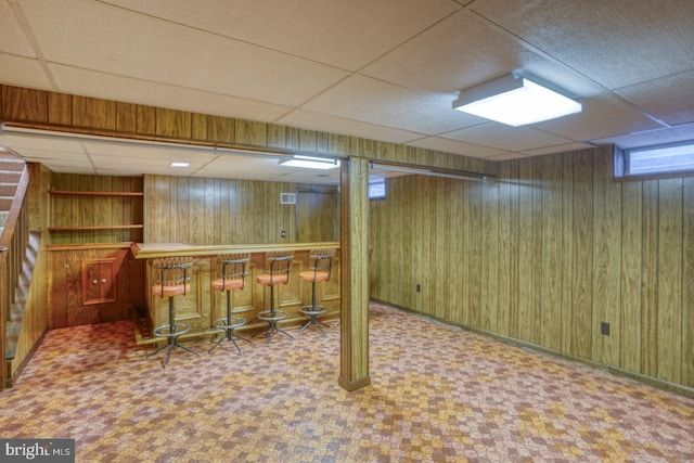 basement featuring a drop ceiling, wooden walls, and bar area