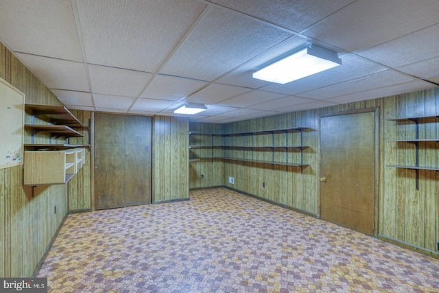 basement featuring wooden walls and a drop ceiling