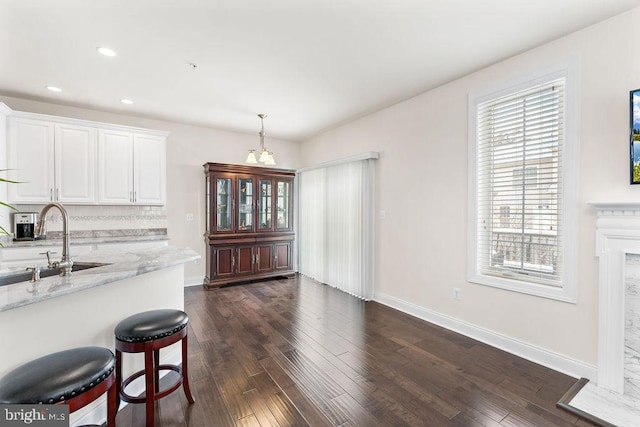 kitchen featuring sink, hanging light fixtures, light stone countertops, dark hardwood / wood-style flooring, and white cabinetry