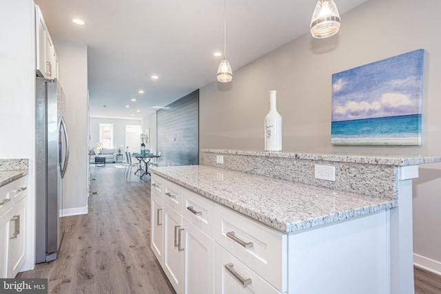 kitchen with white cabinets, decorative light fixtures, light stone counters, and stainless steel refrigerator